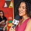 Jornalista Beatriz Oliveira, usa uma camisa rosa e segura um microfone durante reportagem para a Globo