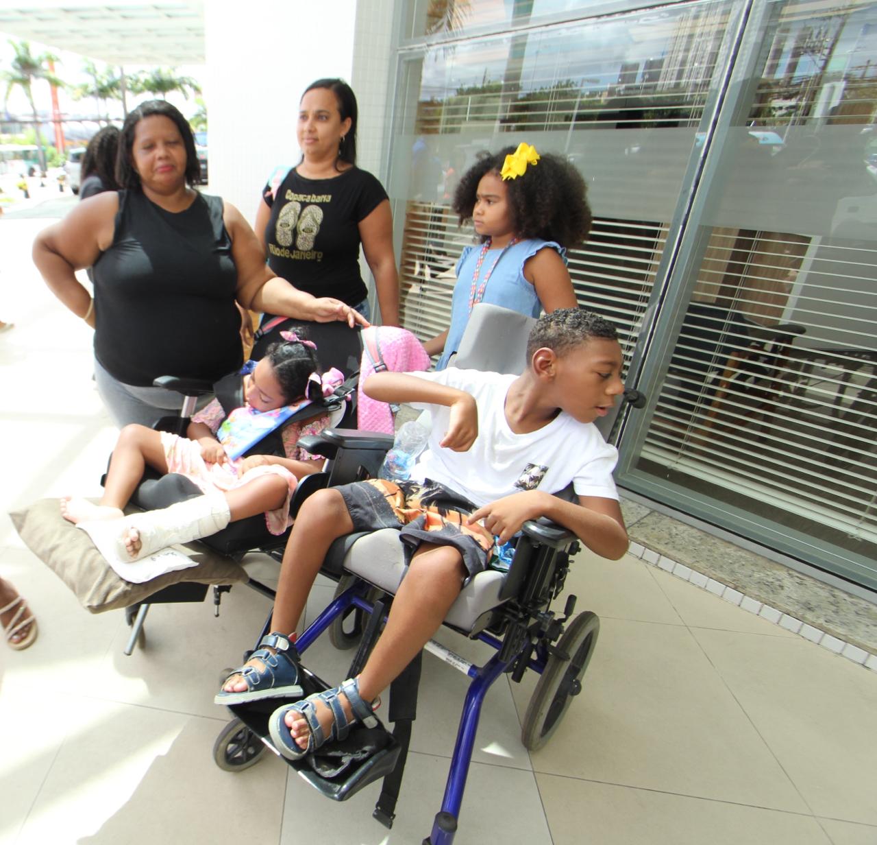 Foto de crianças com microcefalia em cadeira de rodas em frente a um estabelecimento comecial de Salvador